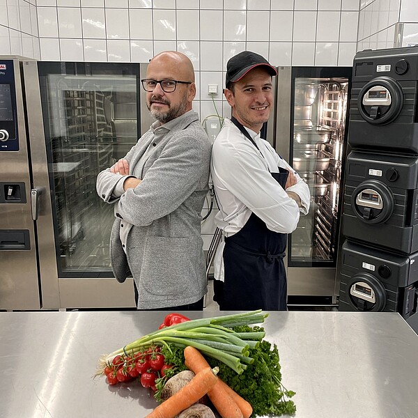 Auf dem Bild sind unser Hoteldirektor & Sous Chef in unserer Catering Küche zu sehen